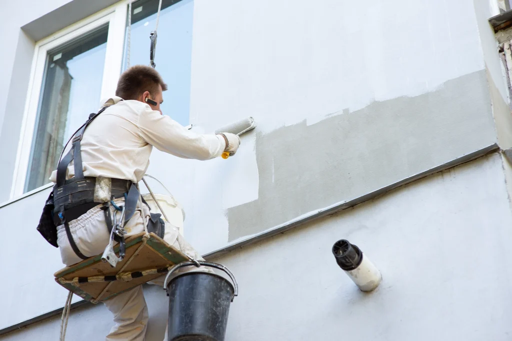 Worker painting the exterior trim beneath a red tile roof above a residential garage door.