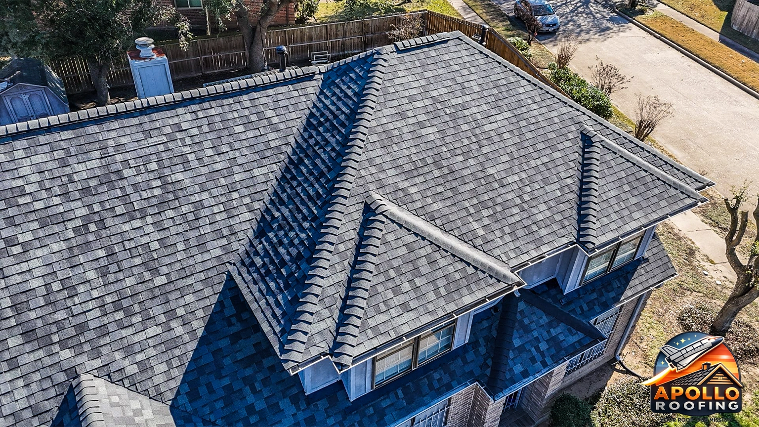 Aerial view of a residential home with a gray asphalt shingle roof, multiple slopes and dormer windows, above a brick and siding exterior.