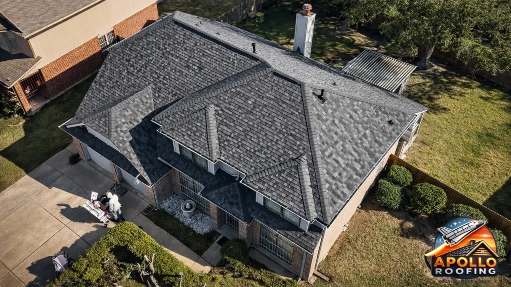 Aerial view of a residential home with a gray asphalt shingle roof, multiple slopes and dormer windows, above a brick and siding exterior.