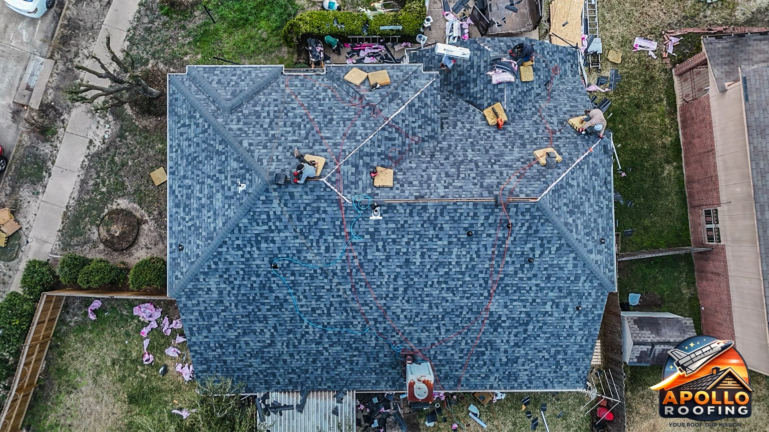 Aerial view of a residential home with a gray asphalt shingle roof, multiple slopes and dormer windows, above a brick and siding exterior.