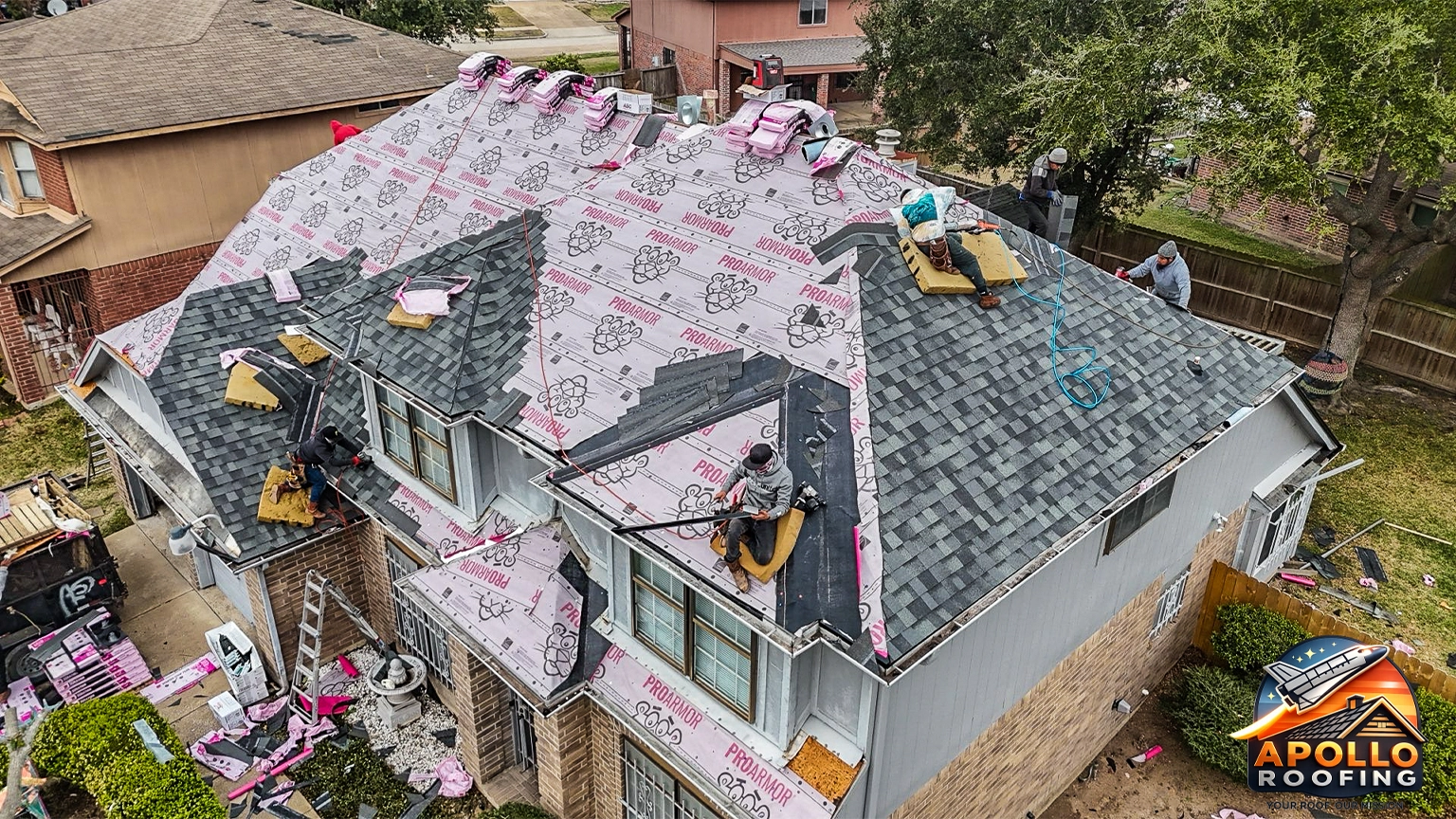 Aerial view of a residential home with a gray asphalt shingle roof, multiple slopes and dormer windows, above a brick and siding exterior.