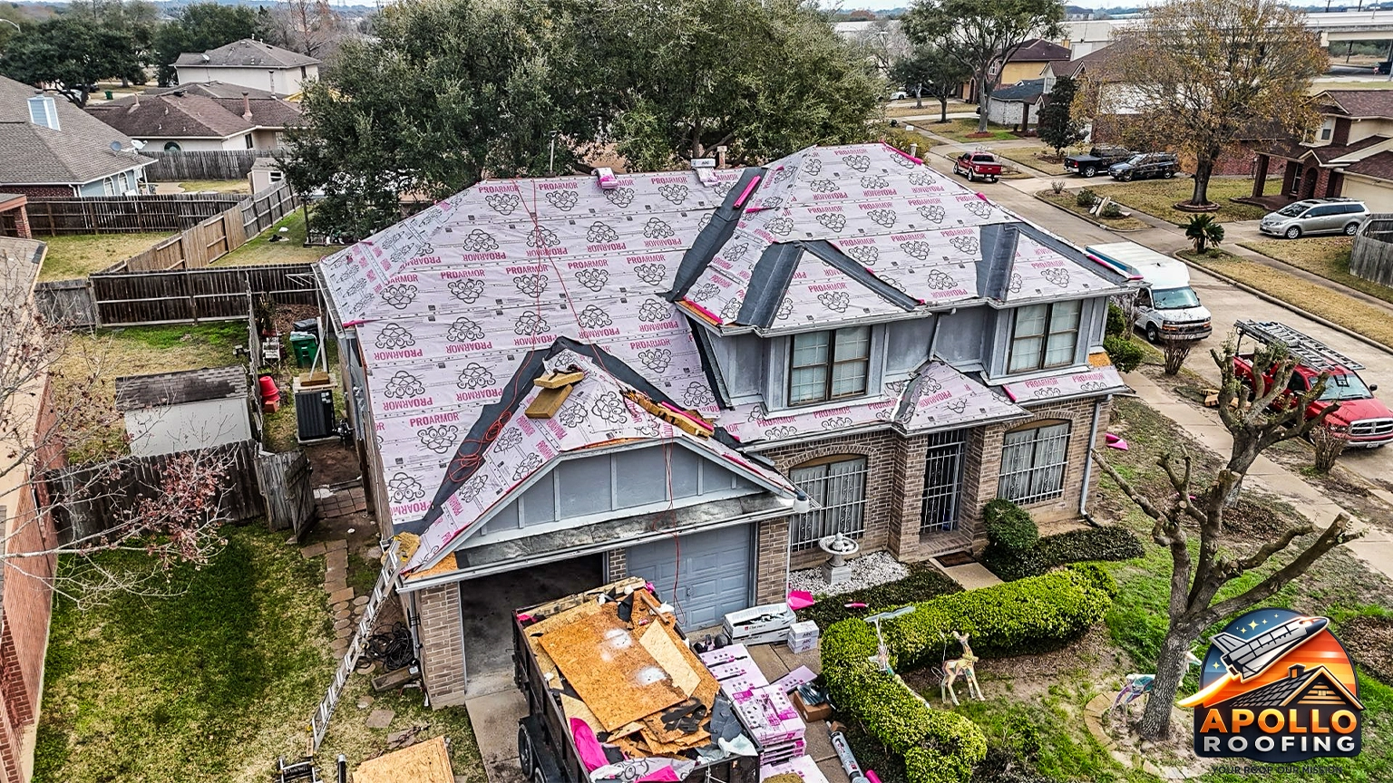 Aerial view of a residential home with a gray asphalt shingle roof, multiple slopes and dormer windows, above a brick and siding exterior.