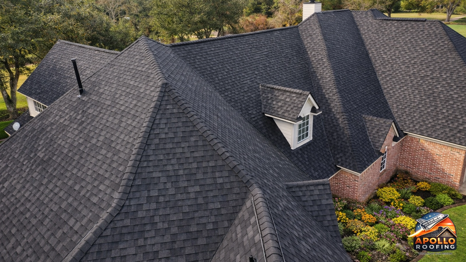Close-up aerial view of a residential roof with dark asphalt shingles, showing multiple ridges, slopes, and roof vents.