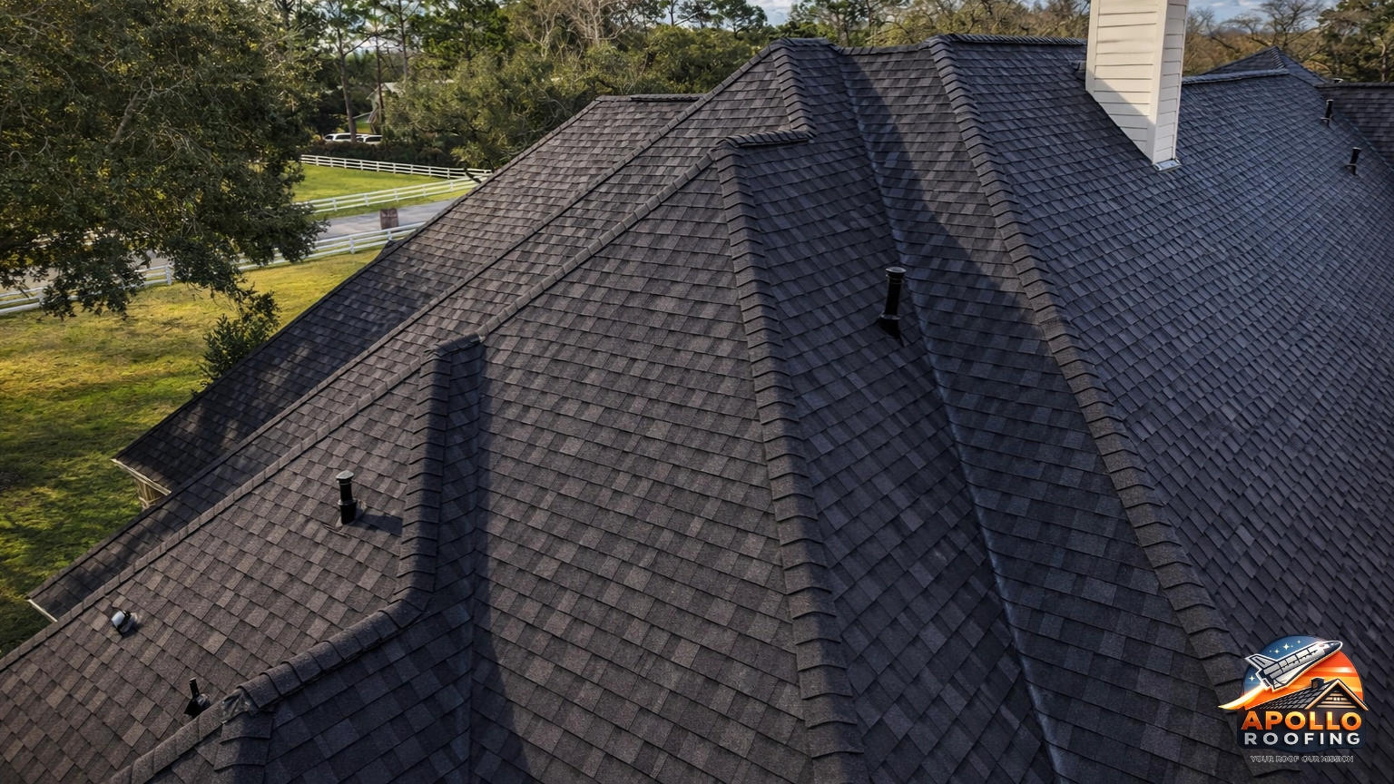 Close-up aerial view of a residential roof with dark asphalt shingles, showing multiple ridges, slopes, and roof vents.